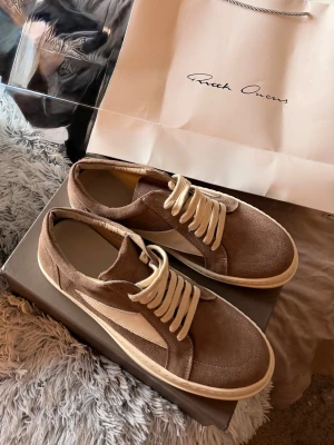 Rick Owens bruna sneakers i mocka - Snygga sneakers från Rick Owens i brun mocka med vita detaljer och vita snören. Skorna har en låg silhuett och en klassisk, chunky sula i vitt. Perfekta för dig som gillar stilrena och trendiga sneakers med premiumkänsla.