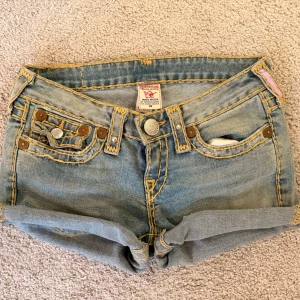 Snygga vintage True Religion jeansshorts - Väldigt lågmidjade. Storlek 26 och 37 cm i midjemått. Har unika detaljer och slitningar som är del av designen. Har själv klippt dom till shorts så det är därför dom är lite ojämna vid kanten. Men på bilderna har jag vikt upp dom och tänker att man ändå vill ha på sig dom så.