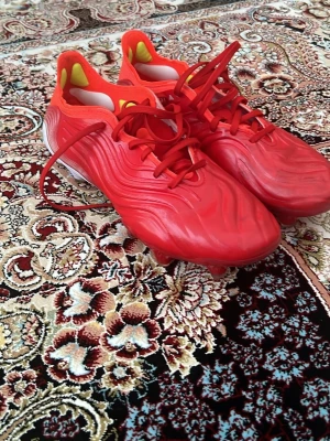Röda Adidas Copa fotbollsskor - Säljer ett par röda Adidas Copa Elite fotbollsskor med snygg vågig struktur på ovandelen. Skorna har snörning, låg profil och gula detaljer på insidan av hälen. Tillverkade i syntetmaterial för bra grepp och kontroll på planen.
