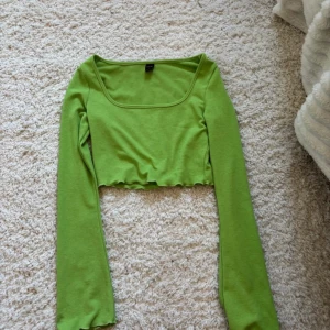 Grön croppad topp med lång ärm - Trendig grön croppad topp med långa ärmar och fyrkantig ringning. Perfekt för dig som vill ha en enkel men snygg bas i garderoben. Tunn och mjuk i materialet, passar till många olika stilar.