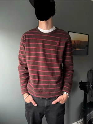 Sweatshirt Blueprint - Säljer en röd sweatshirt ifrån blueprint med tunna rosa ränder och broderad logga på bröstet. Tröjan har rund halsringning och är gjord i mjukt bomullsmaterial. Perfekt för en avslappnad och stilren look.