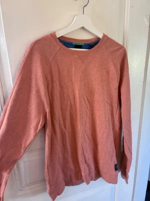Korall sweatshirt från Scotch & Soda - En stilren korall sweatshirt från Scotch & Soda med rund halsringning och långa ärmar. Tröjan har en relaxed fit och är tillverkad i mjukt bomullsmaterial. Perfekt för dig som gillar en enkel men snygg look.