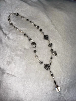 Pärlhalsband med silverfärgade berlocker - Säljer ett halsband som tyvärr inte kommer till användning längre!  Superfint med en ganska urringad tröja 