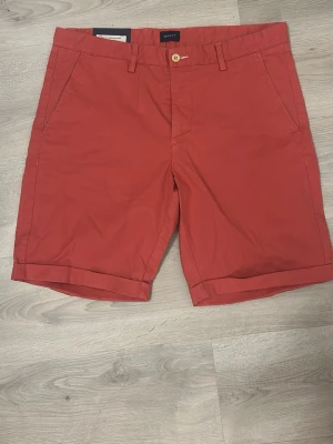 Röda shorts från Gant i bomull - Snygga röda shorts från Gant med klassisk design, uppvikta benslut och fickor både fram och bak. Tillverkade i mjuk bomull och perfekta för sommaren. Stängs med knapp och dragkedja, har hällor för bälte och stilrena detaljer.