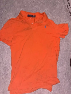 Orange pikétröja från Polo Ralph Lauren - Snygg orange pikétröja från Polo Ralph Lauren, Slim fit-modell med den ikoniska broderade loggan på bröstet. Perfekt för en avslappnad och stilren look.