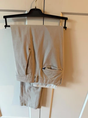 Beige chino  från Boggi Milano - Snygga beige chino från Boggi Milano i klassisk rak modell. Byxorna har diskreta fickor och är tillverkade i ett lätt och bekvämt material som passar perfekt till en dressad look. Stilsäker design med fina detaljer i midjan. Aldrig använd!
