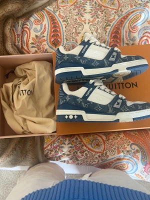 Louis Vuitton trainers - Säljer ett par Louis Vuitton sneakers i blått och vitt med klassiskt monogrammönster. Skorna har låga skaft, vita snören och detaljer i läder och denim. Snygg kontrast mellan blått tyg och vita partier, samt ikoniska LV-symboler på sidan och sulan.