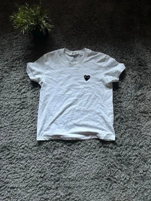 Vit Comme des Garçons Play t-shirt - Vit t-shirt från Comme des Garçons Play med det ikoniska svarta hjärta-trycket på bröstet. Klassisk rund hals och korta ärmar. Tillverkad i mjuk bomull för en skön och avslappnad look.
