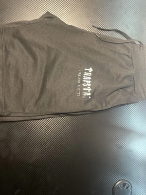 Trapstar shorts -  Koppla av med stil i dessa mjuka och ventilerande svarta shorts. Med en cool Trapstar-grafik är de perfekta för att chilla hemma, springa ärenden eller för lättare träning. Elastisk midja med dragsko för perfekt passform.