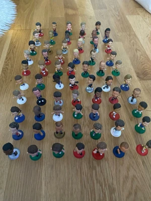 Samling fotbollsspelarfigurer - Stor samling 65 stycken små fotbollsspelarfigurer med olika färger på basen, bland annat röd, grön, blå, vit och guld. Figurerna är gjorda av plast och har detaljerade ansikten och tröjor som liknar riktiga fotbollsspelare. Perfekt för dig som gillar fotboll och samlarobjekt. Zlatan finns med 