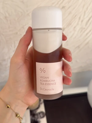 Dr.Ceuracle Kombucha Tea Essence - Vegan Kombucha Tea Essence från Dr.Ceuracle. Tonern kommer i en cylinderformad plastflaska med vit skruvkork och ljusrosa etikett. Innehållet är brunaktigt och flytande, perfekt för att fräscha upp huden och ge lyster.