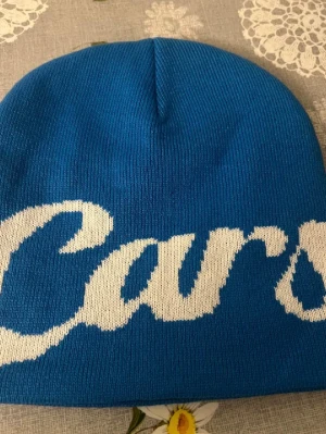 Carsicko mössa - Snygg blå mössa från Carlsicko med vit text i stor, kursiv stil runt hela mössan. Tillverkad i mjukt, stretchigt material som sitter skönt på huvudet. Perfekt accessoar för att addera lite färg till din outfit.