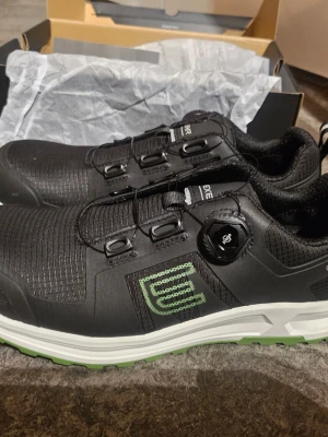 Skyddsskor Exelar strl 43 - Skyddsskor med snörningssystem och grön sula. Skorna är svarta med vita och gröna detaljer. Ett par inläggssulor av märket Footlab Support Stable Trac medföljer strl 40-42. Förp endast öppnade, aldrig provade. Ord. Pris på endast sulor Ca 600:- 