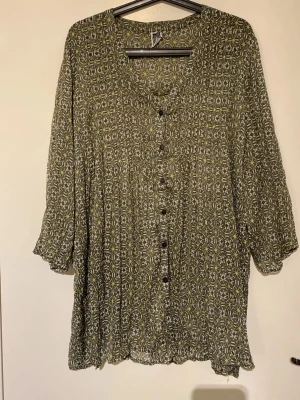 Grön mönstrad blus från Isolde - Snygg grön blus från Isolde med blommigt mönster i vitt och gult. Blusen har knappar framtill, v-ringning och trekvartsärm. Tunt och luftigt material som ger en avslappnad känsla. Perfekt för dig som gillar bohemisk stil.