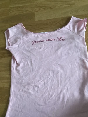 Ljusrosa t-shirt med texttryck - Söt ljusrosa topp med korta ärmar och texten 'Dansar vidare i livet' tryckt framtill. Tillverkad i mjuk bomull och har en enkel, feminin passform. Perfekt för dig som gillar en avslappnad men ändå söt stil. Storleken är 158 men går inte att lägga in på där man trycker in storlek så de skrivs här i beskrivningen.