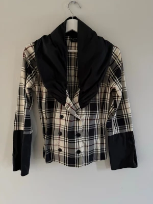 Rutig kavaj med bred krage - Snygg rutig jacka från Summer Time med bred svart krage och svarta detaljer på ärmarna. Bra skick då den kommit till användning fåtal gånger. Storlek xs men skulle säga att den passar s också.