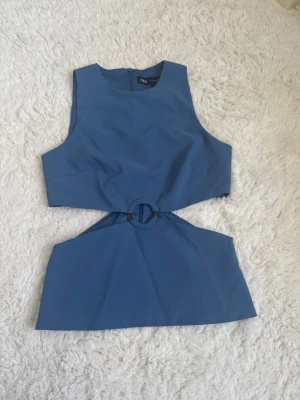 Blå ärmlös topp med ringdetalj Zara - Snygg blå ärmlös topp från Zara med unik ringdetalj i midjan och cut-out design. Toppen har en croppad passform och är perfekt för dig som vill sticka ut lite extra. Materialet känns mjukt och lätt mot huden.