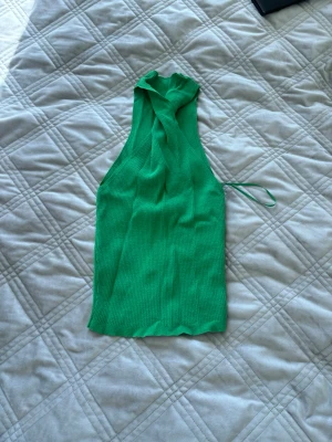 Grön ribbad halterneck linnetopp - Snygg grön ribbad linnetopp med halterneck och knyt i halsen. Toppen är ärmlös och har en tight passform som framhäver axlarna. Perfekt att styla med jeans eller kjol för en trendig look. 