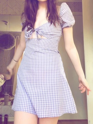 Lila rutig kortklänning med puffärm - Superfin lila och vit rutig kortklänning med puffärmar och söt knytning framtill. Klänningen har en feminin v-ringning och markerad midja. Perfekt för vår och sommar, och ger en romantisk vibe.