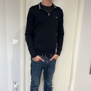 Svart tröja med dragkedja från GANT - Säljer en stilren svart tröja från GANT med dragkedja vid halsen. Tröjan har långa ärmar och en diskret logga på bröstet. Perfekt för en avslappnad och snygg look.