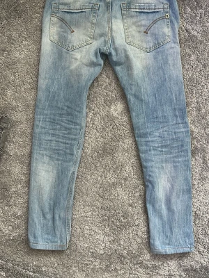 Dondup jeans - Säljer ett par ljusblå dondup jeans med snygga slitningar och tvättade detaljer. Jeansen har två bakfickor med dragkedjedetaljer och klassisk femficksdesign. Perfekta för en avslappnad och trendig look. Jeansen är i använt men ändå bra skick.  självklart äkta