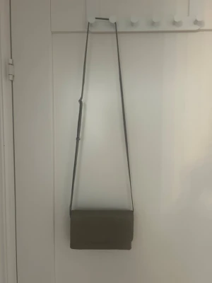 Adax axelväska - Snygg axelväska från Adax i taupefärgat läder med justerbar axelrem. Väskan har en stilren, rektangulär form och lockstängning. Perfekt storlek för det viktigaste och enkel att matcha till olika outfits.