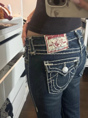 True Religion bootcut jeans mörkblå - Säljer ett par mörkblå bootcut jeans från True Religion med kontrasterande vita sömmar. Midjemått: 39 cm (tvärs över), innerbenet: 82 cm 