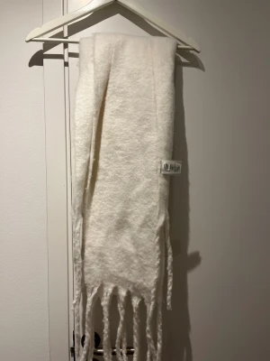 Vit fluffig halsduk med fransar - Mysig och fluffig vit halsduk med långa fransar i ändarna. Tillverkad i en mjuk materialmix som känns lyxig och varm. Perfekt för att hålla sig varm under kalla dagar och ger en clean look till din outfit.