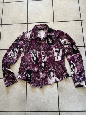 Lila mönstrad skjorta storlek S/M - Unik långärmad skjorta med collage av svartvita porträtt och lila rosor. Skjortan har klassisk krage, knappar framtill och figurnära passform. Perfekt för dig som vill sticka ut med ett konstnärligt och retroinspirerat plagg.