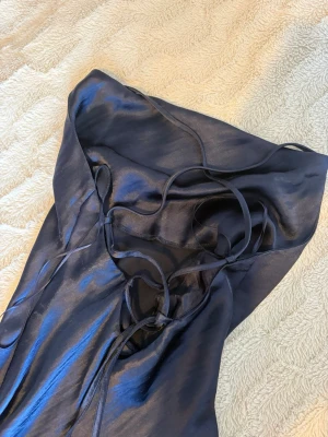 Satin marinblå klänning  - Elegant marinblå långklänning i glansigt sidenliknande material med smala axelband, lätt V-ringning och figurnära passform. Slits nertill. Från ASOS, storlek 32. 