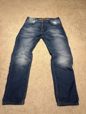 Blå jeans med raka ben - Säljer ett par klassiska blå jeans med raka ben och snygga slitningar. Jeansen har fem fickor, normal midja och kontrastsömmar. Perfekta för en avslappnad och trendig stil. Materialet är mjukt denim som ger en skön känsla hela dagen.