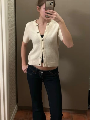 Kortärmad vit cardigan från Gina Tricot - Söt kortärmad cardigan i mjuk vit stickad kvalitet från Gina Tricot. Tröjan har rund halsringning, knappar framtill och ribbade kanter. Perfekt att styla med jeans eller kjol för en enkel och trendig look. Använd fåtal gånger 