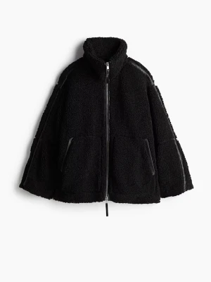 Svart oversized teddyjacka - Mysig svart teddyjacka med hög krage och dragkedja framtill. Jackan har två stora fickor och detaljer i fuskläder längs ärmar och fickor. Perfekt för att hålla värmen och ge en cool, avslappnad look.