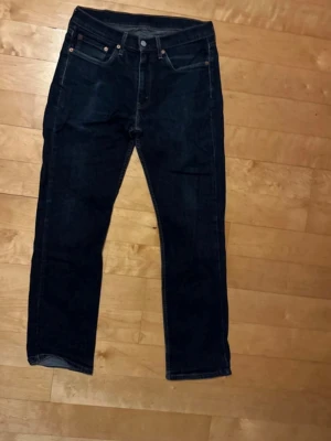 Levi's 514 mörkblå jeans - Säljer ett par klassiska Levi's 514 jeans i mörkblå denim. Modellen har rak passform, fem fickor och snygga kontrastsömmar. Perfekta för dig som gillar tidlös stil och vill ha ett par jeans som funkar till allt. Levi's patch bak och röd etikett vid fickan.