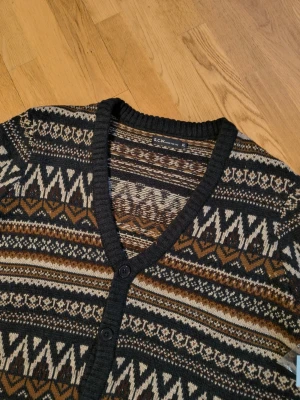 Mönstrad kofta från S.C.W - Säljer en mysig kofta från S.C.W med snyggt mönster i svart, brunt, beige och vitt. Koftan har v-ringning, knäppning framtill med svarta knappar och ribbade muddar. Perfekt för lager på lager och ger en retrovibe till din outfit.