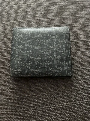 Svart plånbok  - Snygg svart plånbok med det vackra mönstret på utsidan. Plånboken har flera kortfack på insidan och är tillverkad i läder. Perfekt för dig som gillar exklusiva accessoarer och vill ha något unikt i fickan.