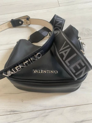 Valentino crossbody väska samt bälte - 🌸Snygg svart crossbody bag från Valentino med justerbar axelrem i nyskick 17x24x7,5 cm.Pris 599kr🌸Helt ny Valentino bälte. 108cm. Pris 299kr.🌸Paketpris 699kr. Finns i Bandhagen alt skickas.