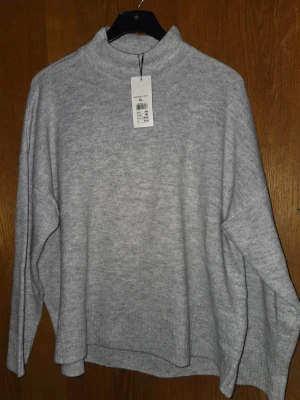 Ljusgrå stickad polotröja XL - Mysig ljusgrå stickad polotröja med diskret glitter i materialet. Tröjan har en lös passform, lång ärm och ribbade muddar. Perfekt för dig som gillar en enkel men ändå lite extra look.