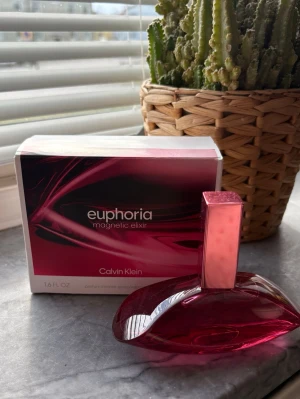Calvin Klein Euphoria Magnetic Elixir - En elegant parfym från Calvin Klein, Euphoria Magnetic Elixir. Flaskan har en djup rosa färg och en unik, böjd form med ett matchande rosa lock. Förpackningen är stilren i svart och rosa med metalliska detaljer. Perfekt för dig som gillar exklusiva dofter. 50ml, ny