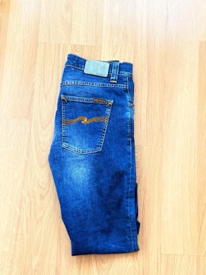 Blå  jeans från Nudie Jeans - Säljer ett par snygga nudie jeans i färgen bay blue, byxorna är i gott skick och storleken 28/32.  Midje mått 38cm  Total längd 103cm  Benöppningen 16cm