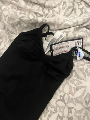 Svart body med smala axelband - Snygg svart body från new yorker med smala axelband och lätt rynkning vid bysten. Tillverkad i ett mjukt och stretchigt material som sitter skönt mot kroppen. Perfekt att styla med jeans eller kjol för en clean look. Endast testat fåtal gånger 