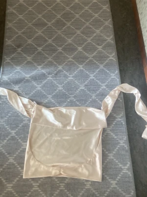 Champagnefärgad satin halterneck topp - Snygg champagnefärgad halterneck topp i satin med draperad urringning och knyt i ryggen. Perfekt för dig som vill ha en trendig och elegant look. Materialet är glansigt och mjukt, vilket ger en lyxig känsla.