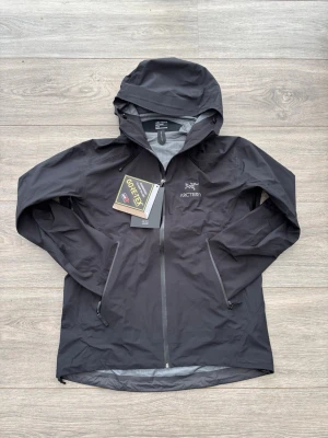 Arc'teryx Gortex Jacka - Snygg svart regnjacka från Arc'teryx i herrmodell, tillverkad i slitstark och vattentät Gore-Tex. Jackan har huva, hel dragkedja framtill och två dragkedjeförsedda fickor. Perfekt för regniga dagar och outdoor-äventyr. Kvitto finns på bild men är borttappad. Storlek M. Funkar perfekt till vandring, regn, skidåkning och mycket mer. 