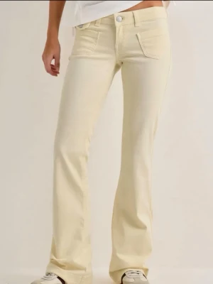 Ljusgula bootcut jeans - Snygga ljusgula bootcut jeans med låg midja och klassiska fem fickor. Jeansen har silverfärgade knappar och är tillverkade i ett mjukt denimtyg som ger en skön passform. Perfekta för dig som vill sticka ut med en ljusare look.