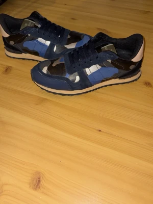 Valentino Rockrunners - Snygga RockRunners från Valentino med blå, svart och grå kamouflagemönster. Skorna har svarta mockadetaljer, svarta sulor och klassisk låg siluett. Perfekta för dig som vill sticka ut med exklusiv streetstyle. Skorna har använts enbart under vintern och har inga större tecken på användning, kanske lite smutsiga bara. Tvättar man dem ser de som nya ut! Priset är ej hugget i sten så var inte rädda att ställa frågor!😁