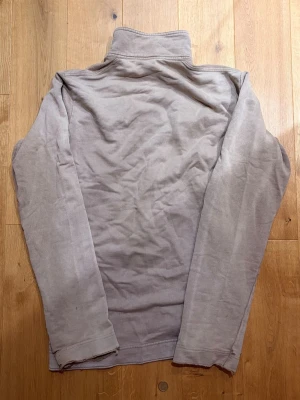  Vintage långarmad tröja från Diesel - Säljer en beige vintage långärmad tröja från Diesel med hög krage och snygga detaljer i form av metallknappar med diesel loggan samt ett märke på bröstet. Tröjan är i mjukt material och har en enkel, stilren design som passar perfekt till jeans eller chinos. Från 90 - talet så har lite tecken av användning på sina ställen mest märkbart på slutet av armarna som är lite fransiga.