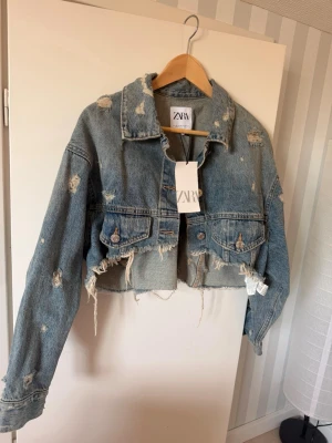 Cropped jeansjacka från ZARA - .Jeansjacka med klassisk krage och knäppning framtill. Modellen passar både dig som vanligtvis bär storlek S eller M. Jackan är helt oanvänd och i nyskick.