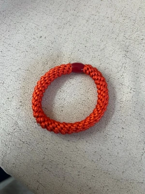 Rött flätat armband från LANVIN - Snyggt armband från LANVIN i starkt röd färg. Armbandet är flätat av glansigt snöre och har en rund röd pärla med ingraverad logga som detalj. Perfekt accessoar för att addera färg till din outfit.