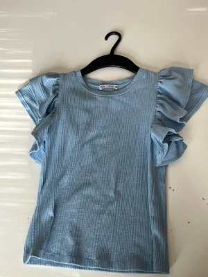 Ljusblå ribbad topp med volangärmar Zara - Supersöt ljusblå topp från Zara med ribbad struktur och stora volangärmar. 