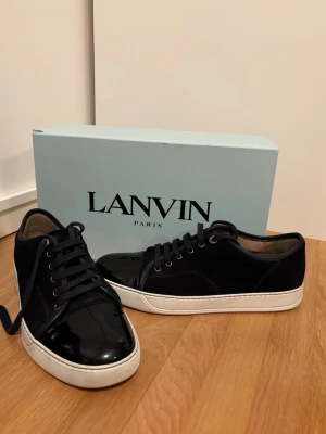 Mörkblåa Lanvin sneakers i mocka och lack - Snygga mörkblåa sneakers från Lanvin med ovandel i mocka och lackdetaljer på tån. Skorna är köpta ifrån farfetch. De är fortfarande i mycket bra skick.